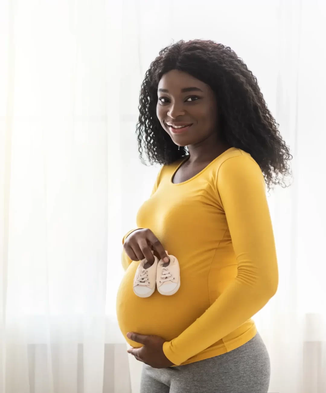 happy-african-expecting-woman-showing-small-shoes-2023-11-27-05-31-05-utc